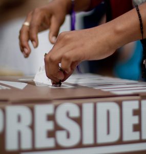 Mano deposita voto en una urna electoral etiquetada "presidente"