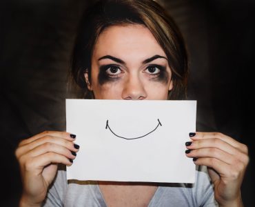 Mujer con rimel corrido por llorar sostiene cartel con sonrisa.